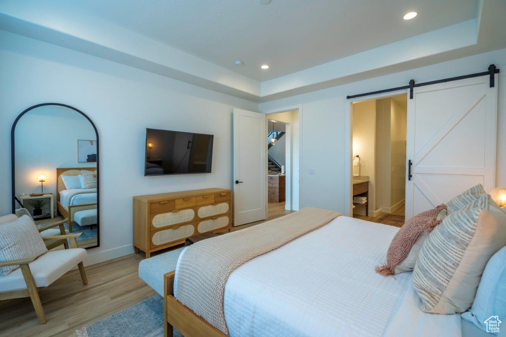 Bedroom with light wood-type flooring, a raised ceiling, a barn door, recessed lighting, and baseboards
