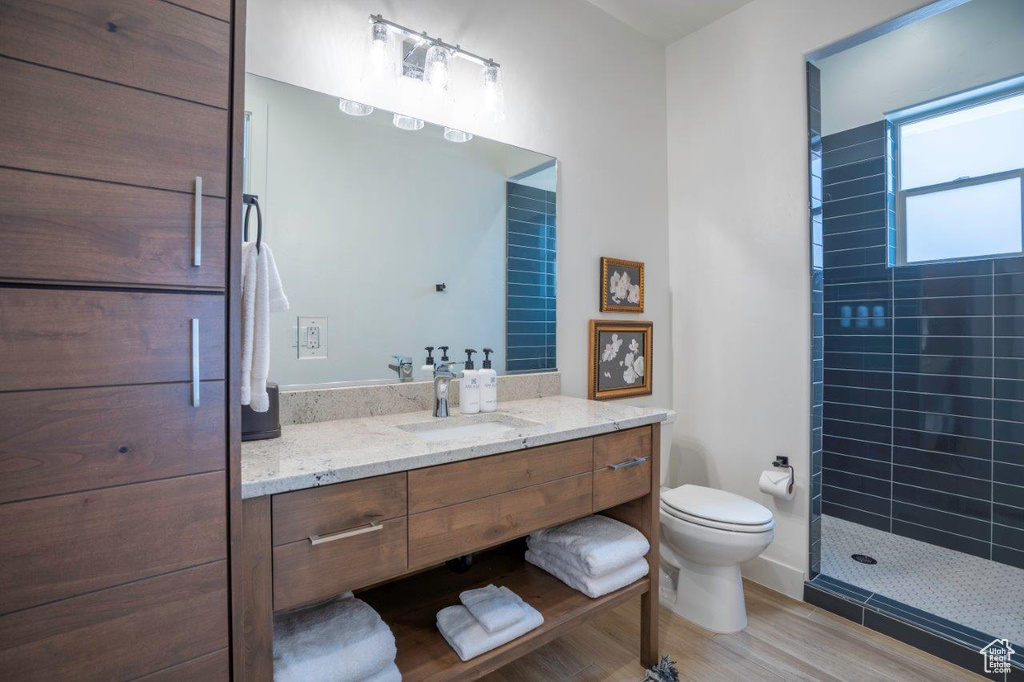 Bathroom featuring vanity, tiled shower, toilet, and wood finished floors