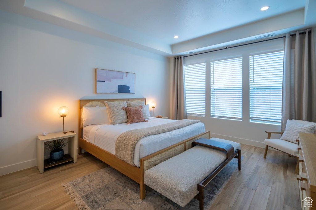 Bedroom with a raised ceiling, baseboards, light wood-style flooring, and recessed lighting