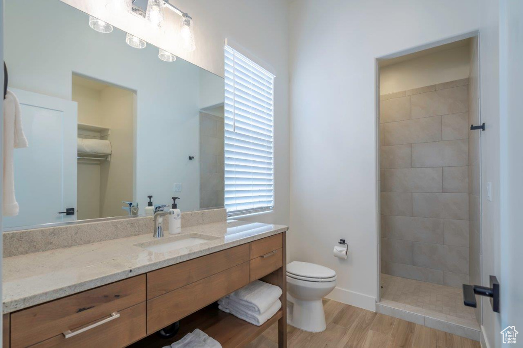 Bathroom featuring vanity, toilet, tiled shower, wood finished floors, and plenty of natural light