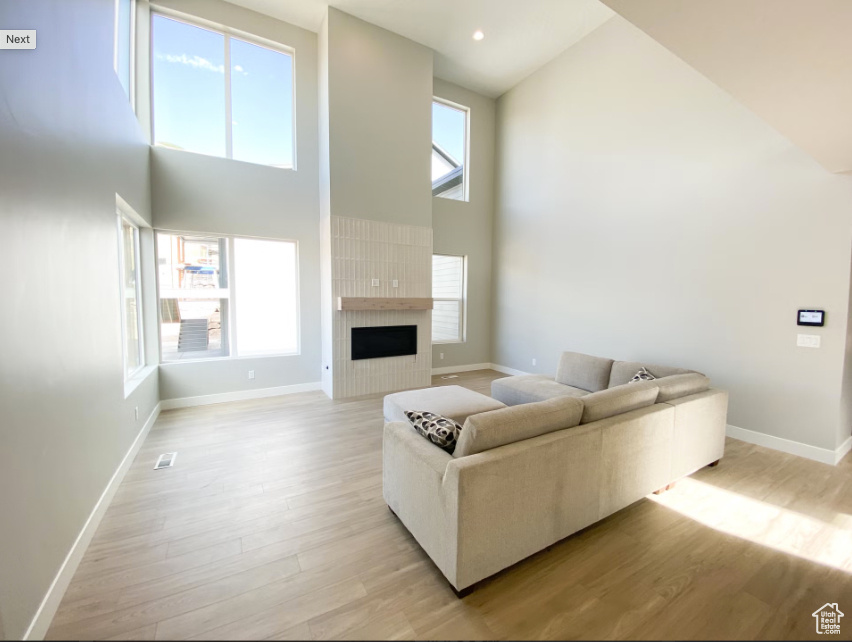 Living room featuring high vaulted ceiling, light wood-style flooring, baseboards, and a large fireplace
