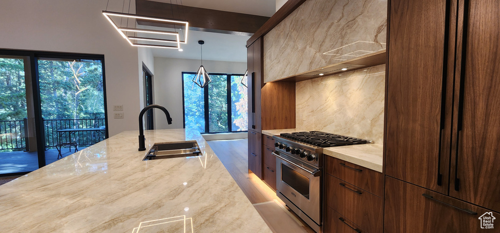Kitchen with high end stainless steel range, a sink, modern cabinets, light stone counters, and backsplash