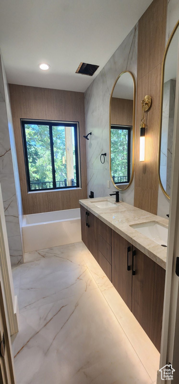 Bathroom featuring marble finish floors, a bathtub, double vanity, and recessed lighting