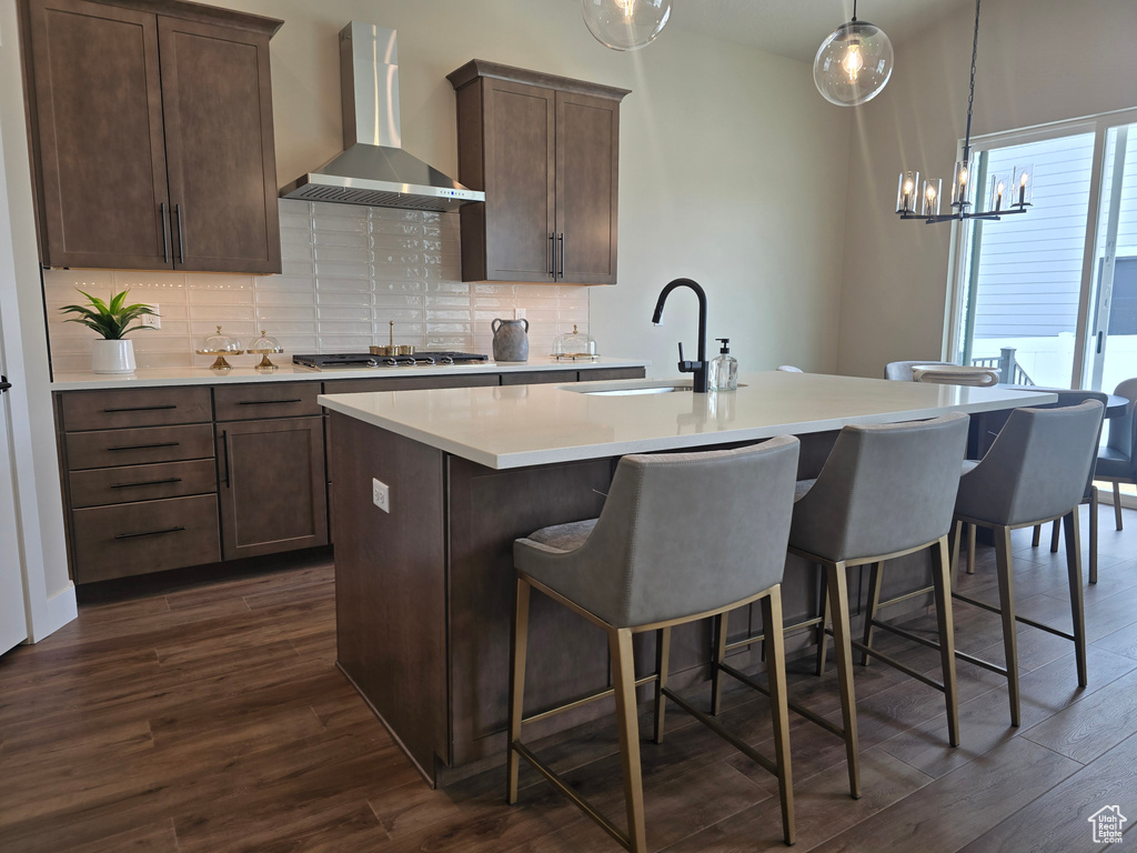 Kitchen featuring wall chimney exhaust hood, a sink, a kitchen island with sink, and dark wood-style flooring