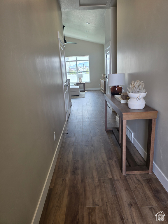Hall featuring vaulted ceiling, dark wood finished floors, baseboards, and attic access