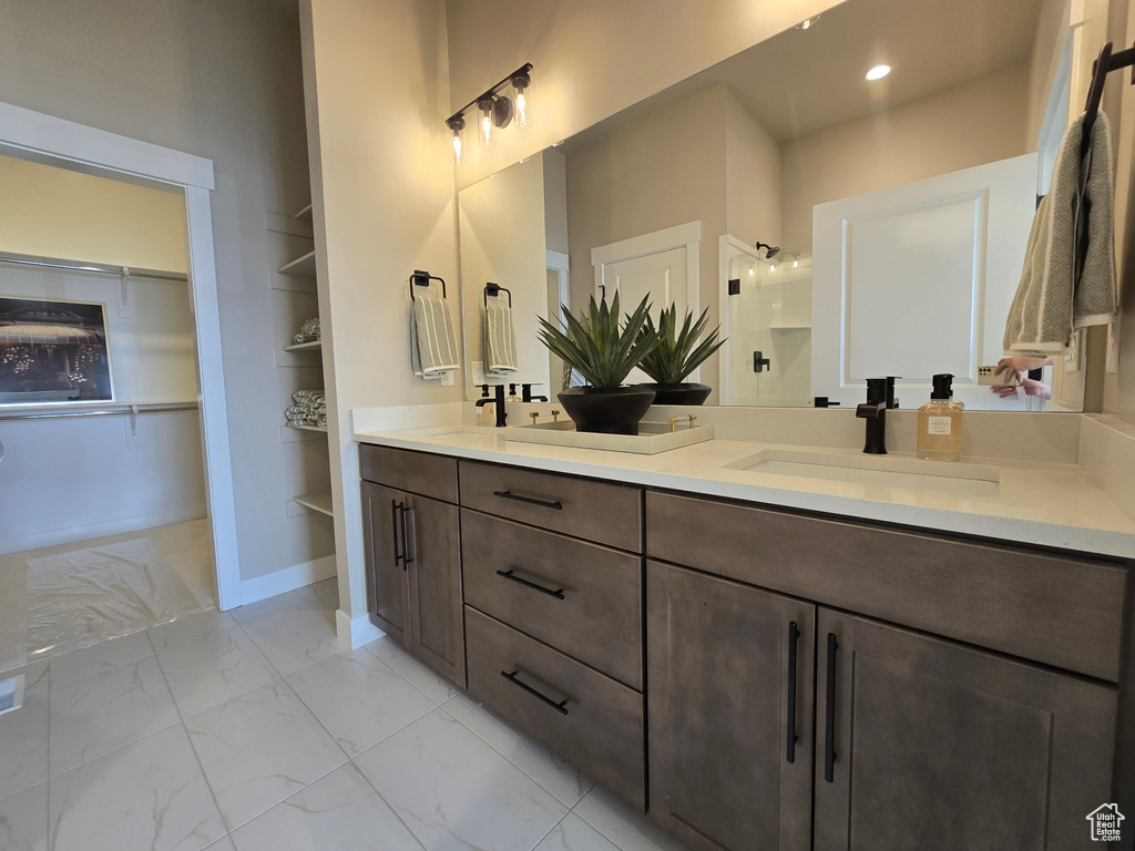 Bathroom featuring marble look tile flooring, double vanity, a shower with door, a walk in closet, and built in shelves
