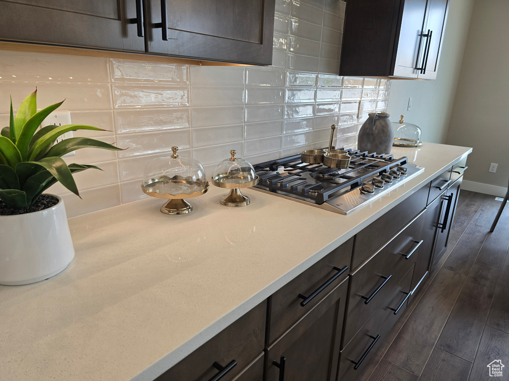 Kitchen featuring stainless steel gas stovetop, decorative backsplash, dark wood-style flooring, light countertops, and baseboards