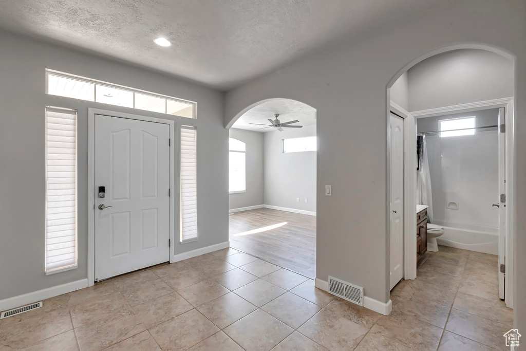 Entryway featuring arched walkways, light tile patterned flooring, a textured ceiling, ceiling fan, and baseboards