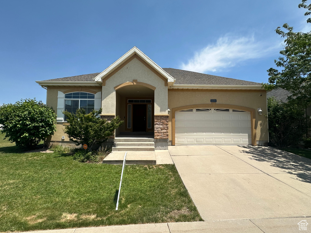View of front facade with an attached garage, driveway, stucco siding, a front yard, and stone siding