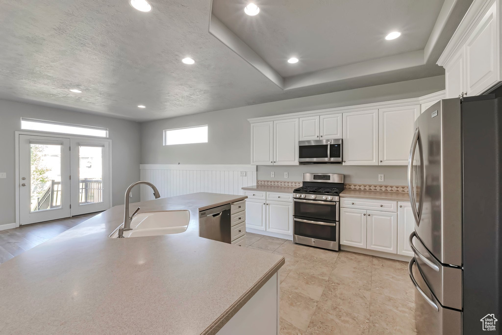 Kitchen featuring appliances with stainless steel finishes, a sink, white cabinetry, a wainscoted wall, and light countertops