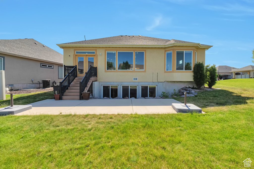 Rear view of house featuring stucco siding, central AC unit, a patio area, a yard, and roof with shingles