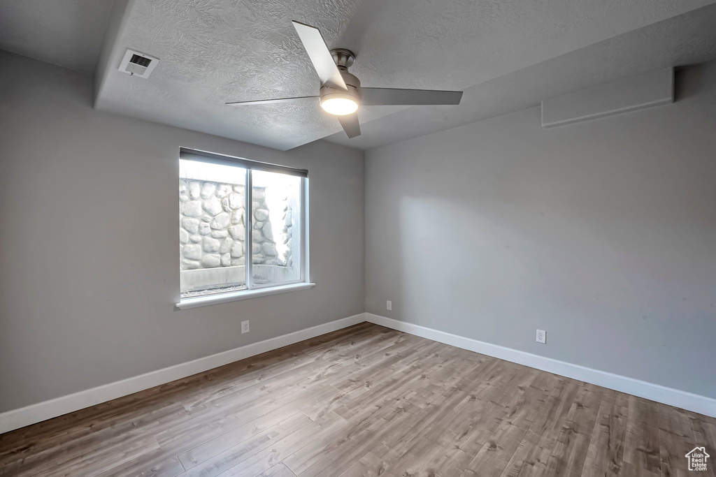 Empty room with wood finished floors, ceiling fan, a textured ceiling, and baseboards