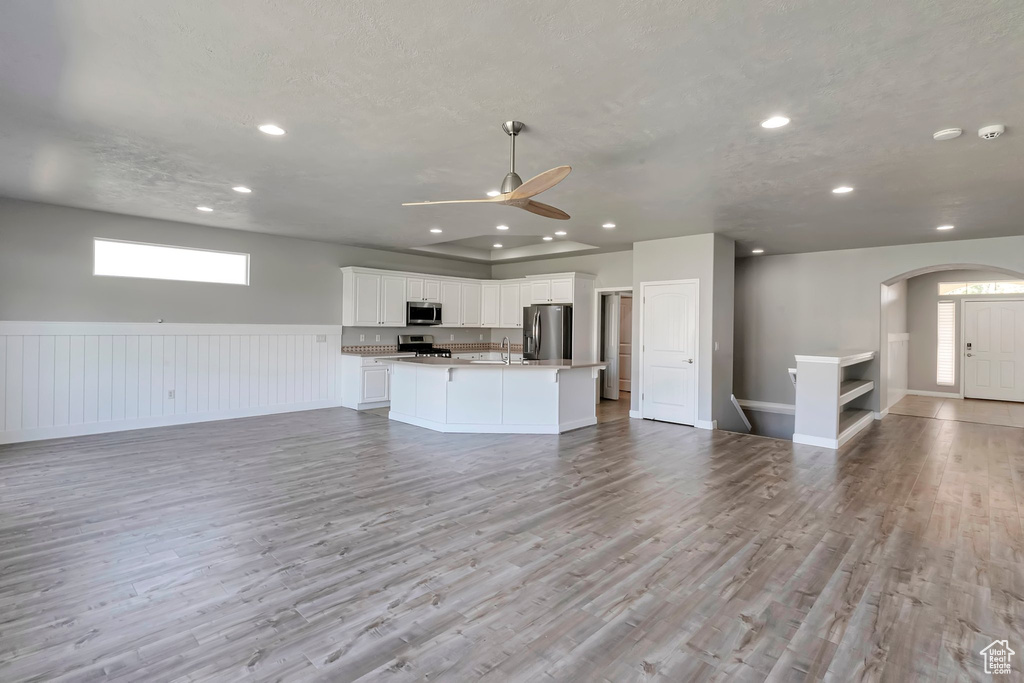 Unfurnished living room featuring ceiling fan, a sink, recessed lighting, arched walkways, and light wood finished floors