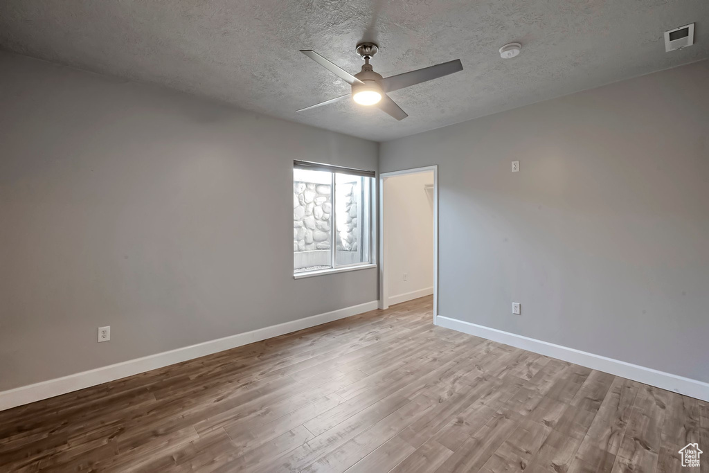 Spare room with wood finished floors, baseboards, a ceiling fan, and a textured ceiling