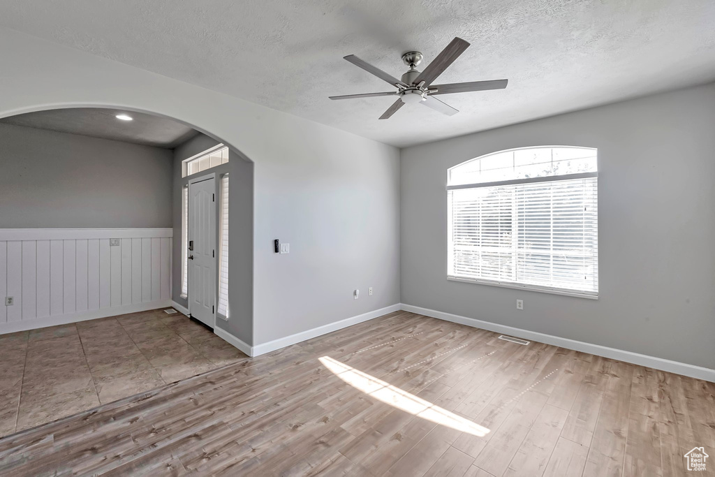 Unfurnished room featuring arched walkways, wood finished floors, a textured ceiling, ceiling fan, and baseboards