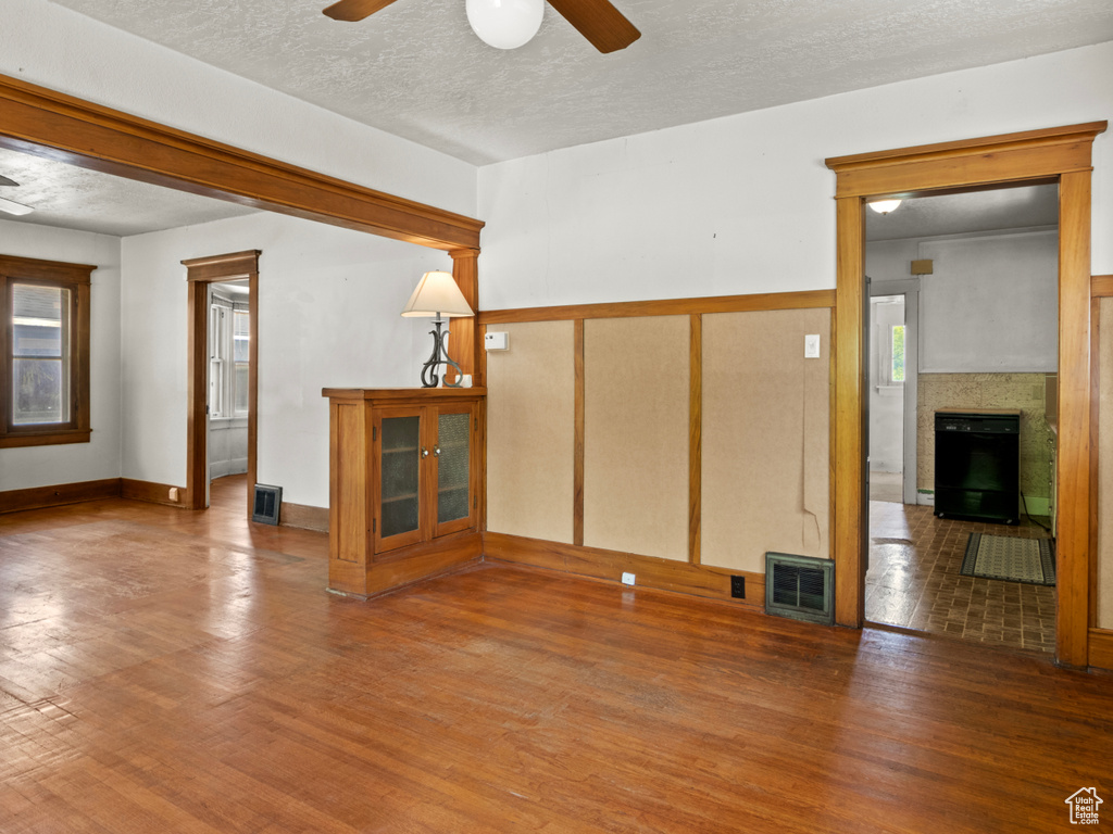 Unfurnished living room with a ceiling fan, wood finished floors, a fireplace, and a textured ceiling