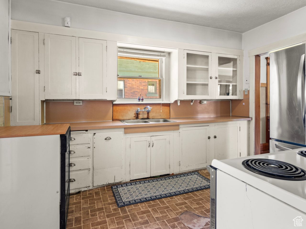 Kitchen featuring a sink, white electric range oven, freestanding refrigerator, white cabinets, and brick patterned floors