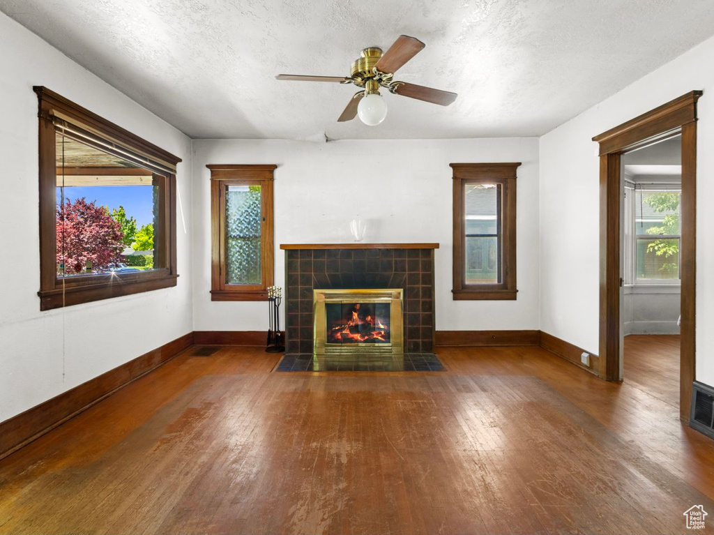 Unfurnished living room with wood finished floors, baseboards, a tiled fireplace, a textured ceiling, and a ceiling fan