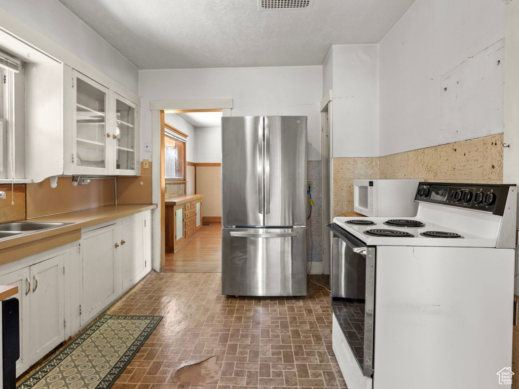Kitchen with white appliances, a sink, white cabinetry, brick patterned floors, and glass insert cabinets