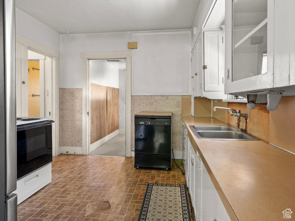 Kitchen featuring dishwasher, a sink, brick patterned flooring, white cabinets, and electric range