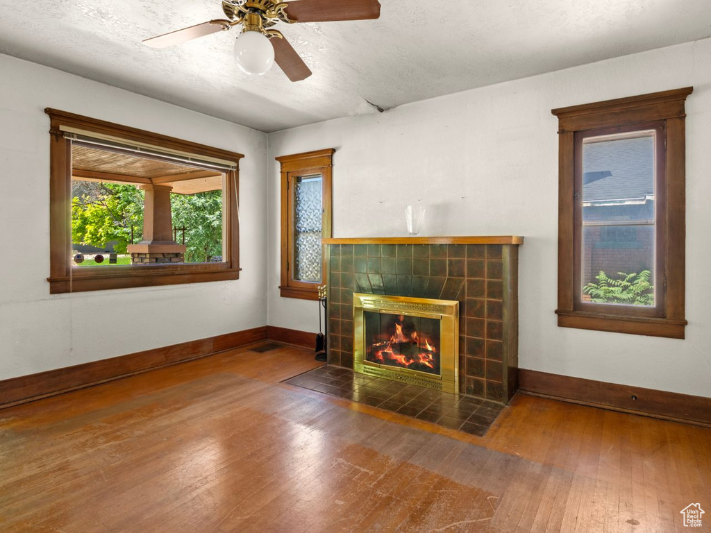 Unfurnished living room with baseboards, wood-type flooring, a tiled fireplace, and ceiling fan