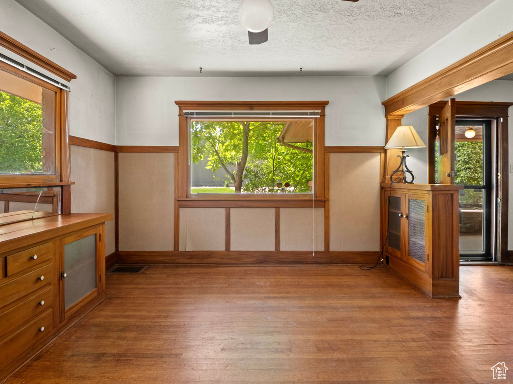 Unfurnished dining area featuring hardwood / wood-style flooring, baseboards, a textured ceiling, and a ceiling fan