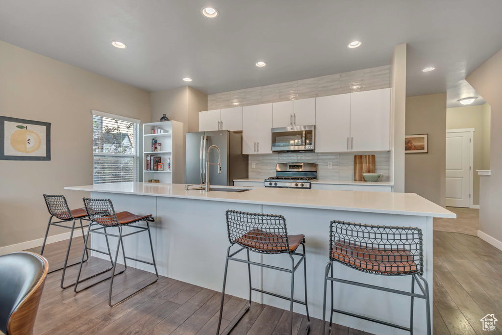 Kitchen featuring stainless steel appliances, a sink, wood finished floors, baseboards, and decorative backsplash