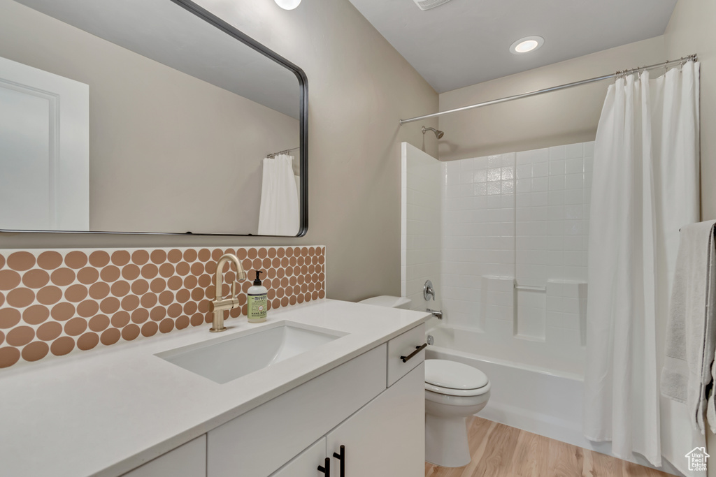 Bathroom with toilet, shower / bathtub combination with curtain, vanity, tasteful backsplash, and wood finished floors