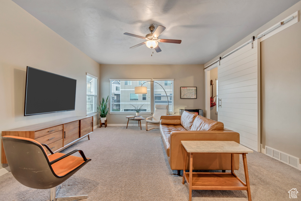 Living room with light carpet, a barn door, a ceiling fan, and baseboards