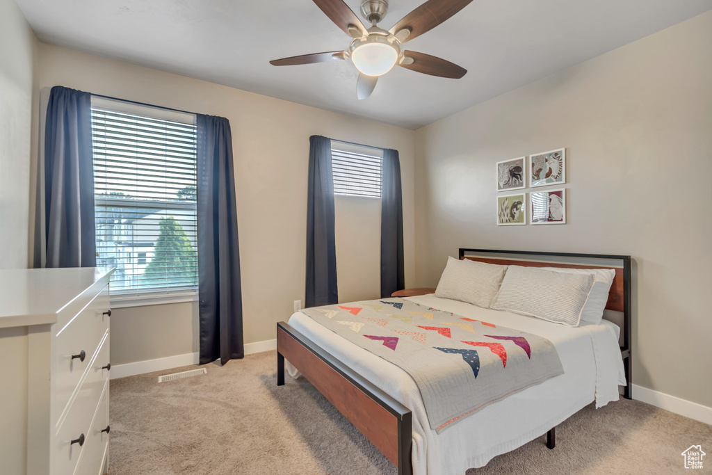 Bedroom featuring multiple windows, light colored carpet, baseboards, and a ceiling fan