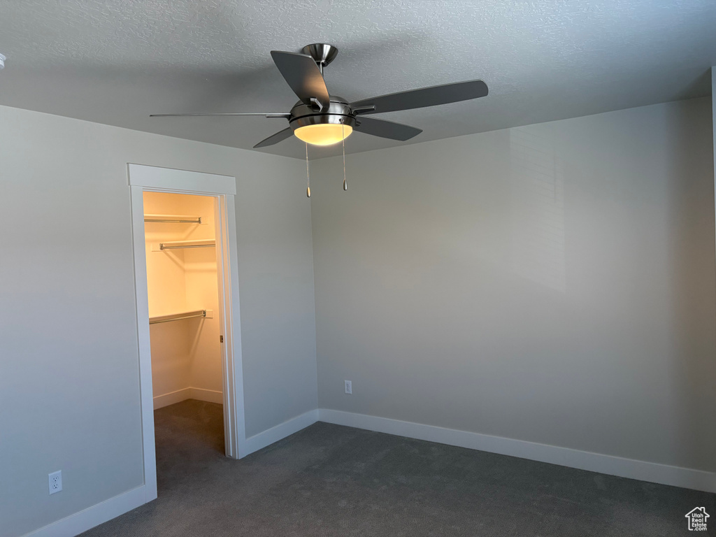 Unfurnished bedroom with a walk in closet, dark colored carpet, a textured ceiling, baseboards, and ceiling fan