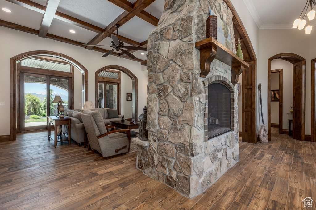Living room featuring arched walkways, wood-type flooring, baseboards, a ceiling fan, and beam ceiling