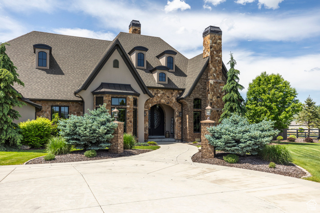 View of front of home with a chimney, roof with shingles, stone siding, and stucco siding
