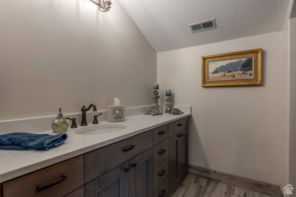 Bathroom with lofted ceiling, wood finished floors, vanity, and baseboards
