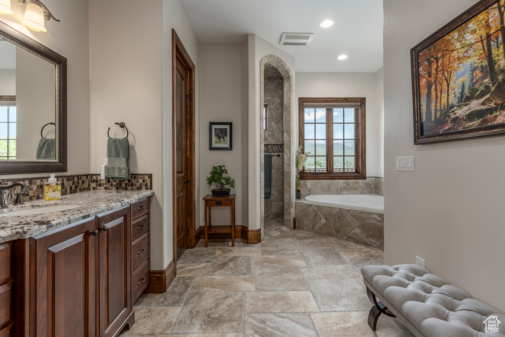 Bathroom featuring a bath, vanity, baseboards, tasteful backsplash, and stone finish floors