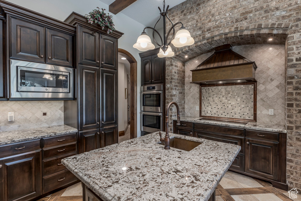 Kitchen featuring appliances with stainless steel finishes, a sink, light stone countertops, arched walkways, and tasteful backsplash