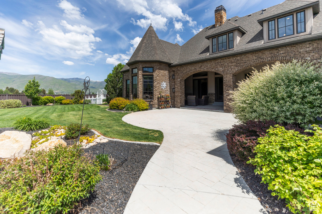 Doorway to property featuring brick siding, a mountain view, a chimney, roof with shingles, and a lawn