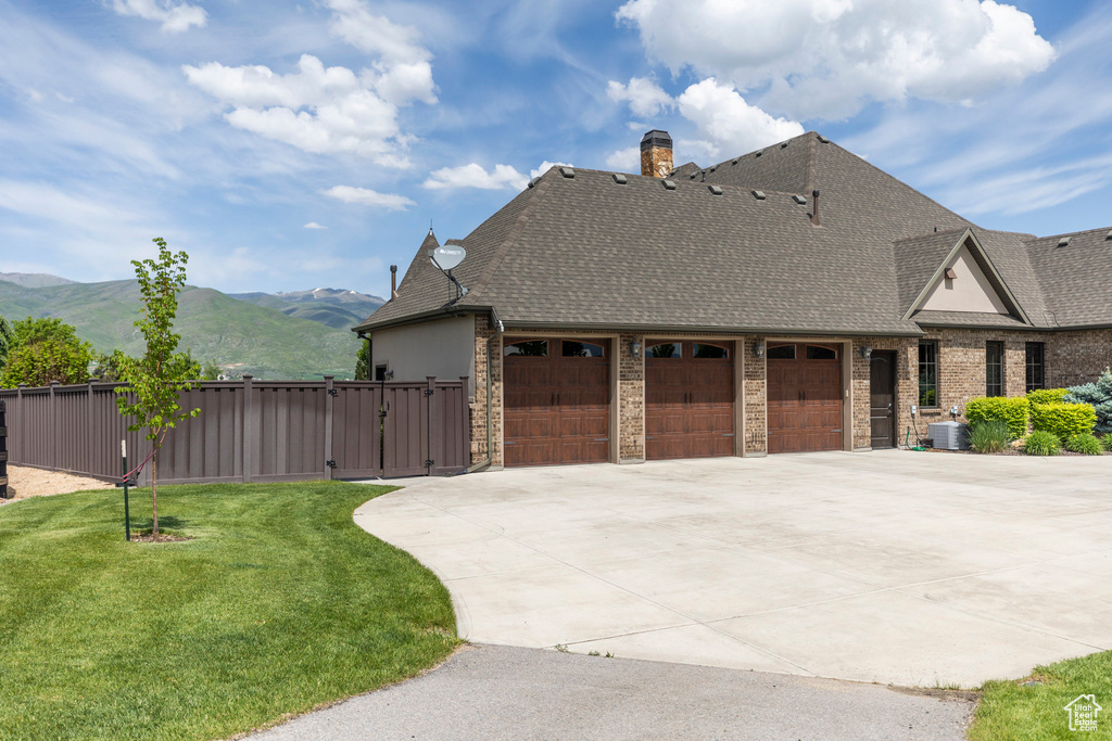 View of home's exterior featuring driveway, an attached garage, a shingled roof, a mountain view, and a gate