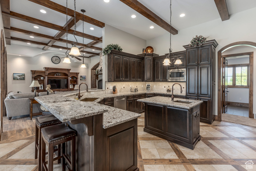 Kitchen featuring stainless steel appliances, a sink, beamed ceiling, inlaid floor details, and tasteful backsplash