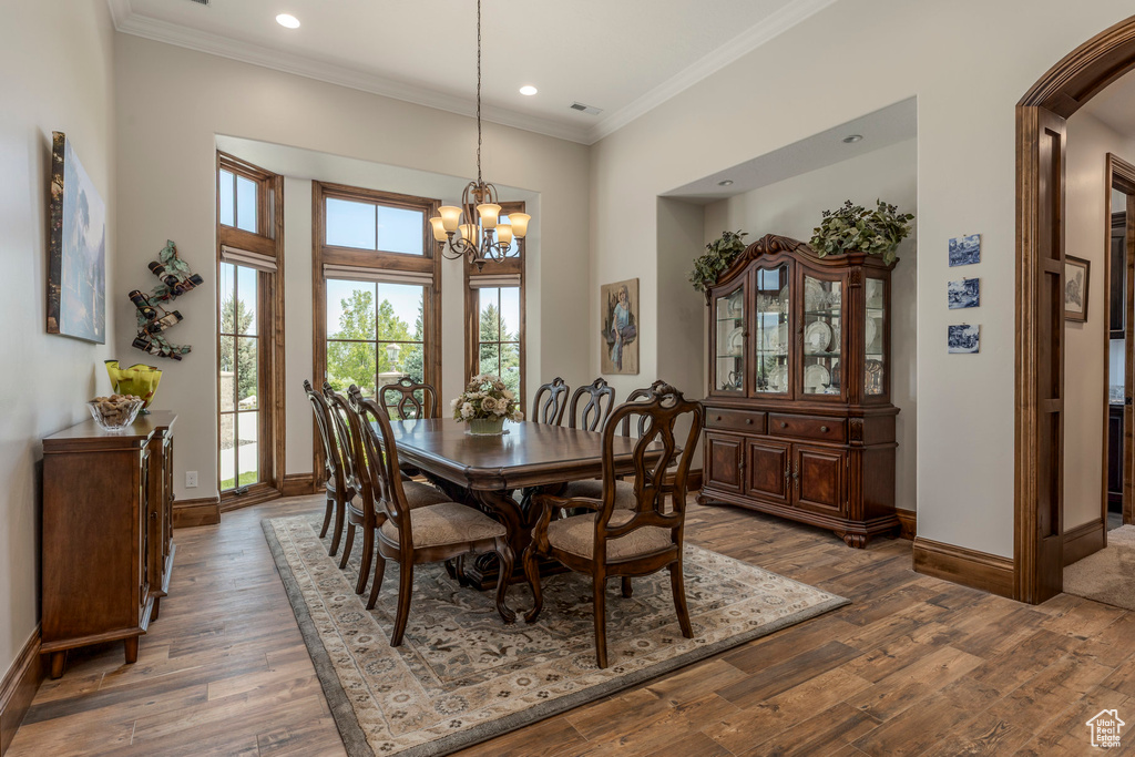 Dining area with a chandelier, baseboards, wood finished floors, crown molding, and recessed lighting