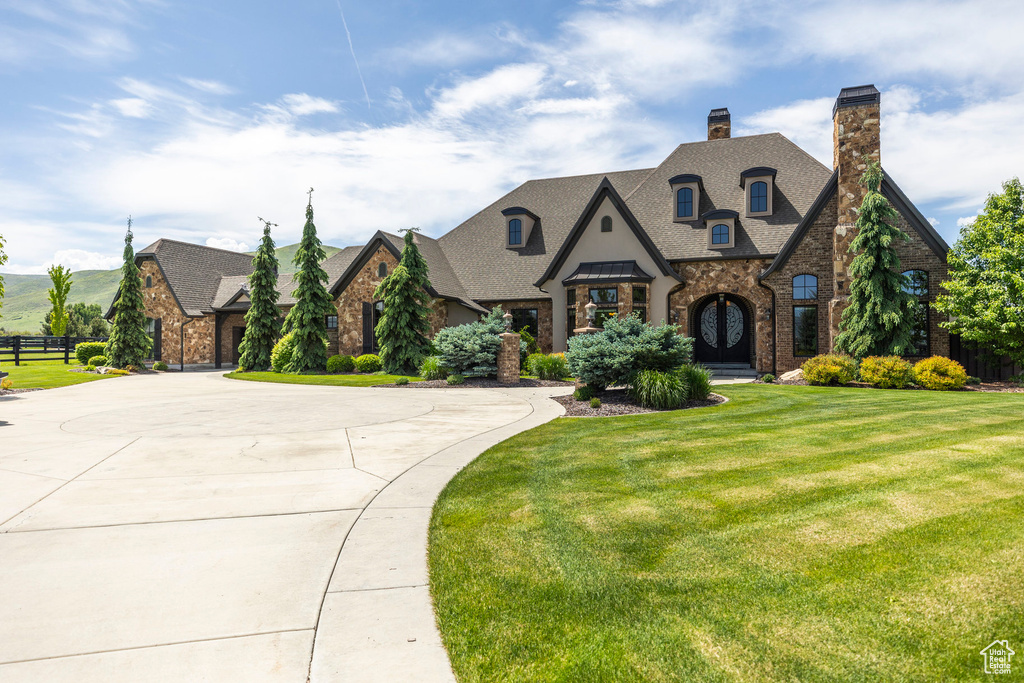 French country home with stone siding, a chimney, curved driveway, and a shingled roof