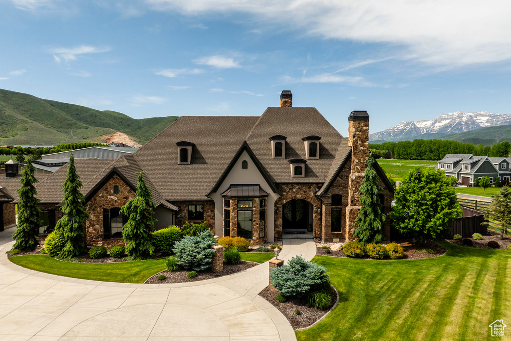 French country style house with stone siding, a chimney, a mountain view, and a front lawn