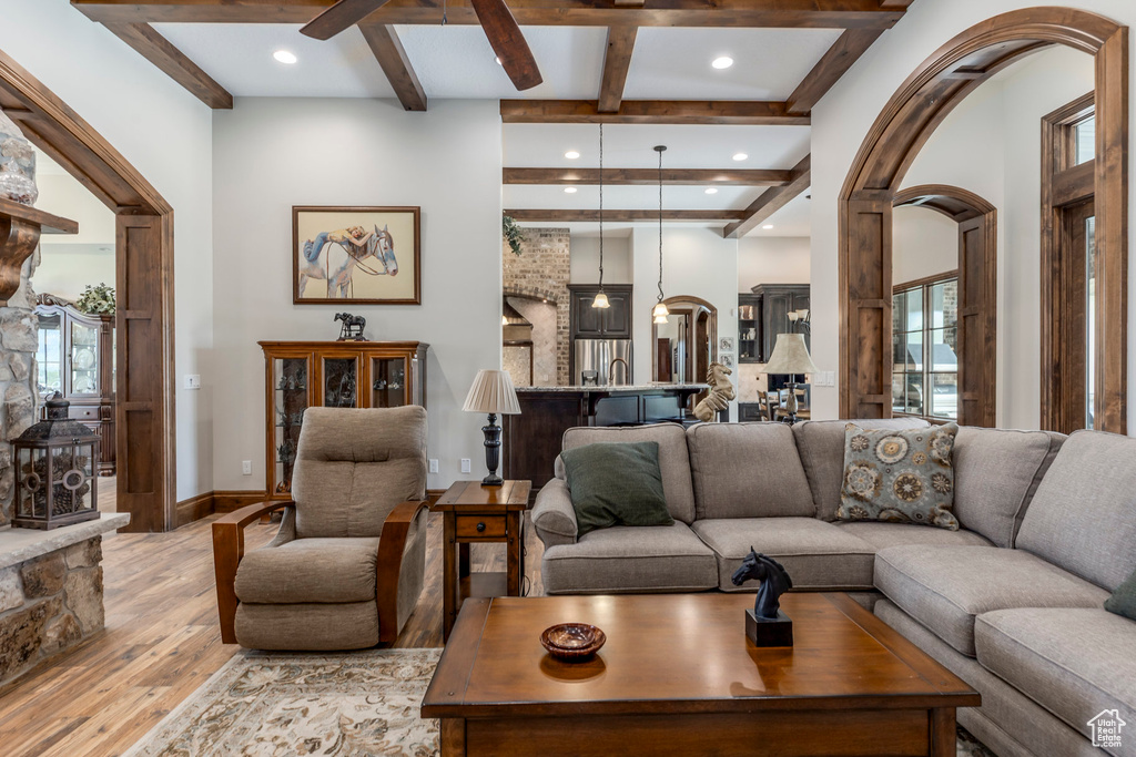Living room with light wood-style floors, arched walkways, beam ceiling, coffered ceiling, and plenty of natural light