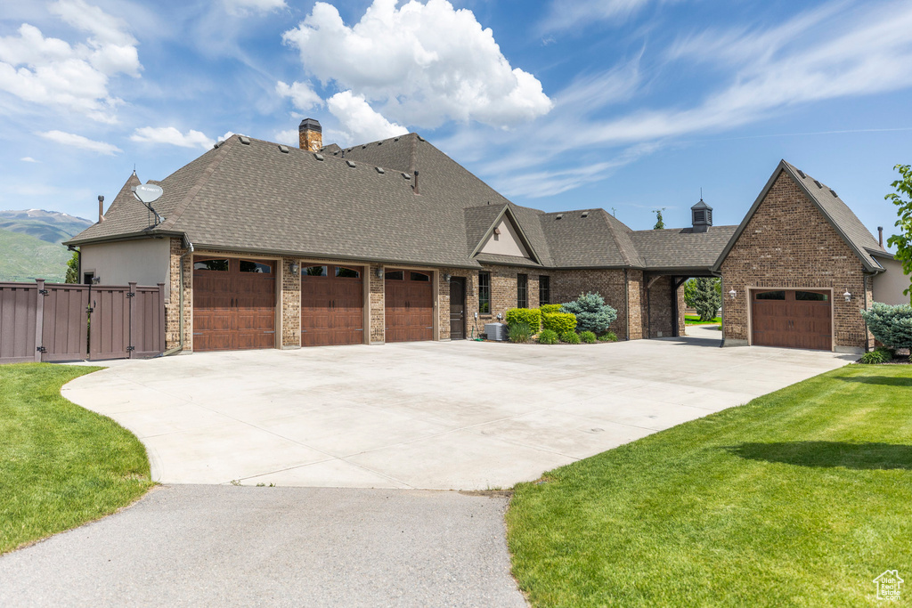 View of front of home with an attached garage, concrete driveway, a shingled roof, a gate, and a front lawn