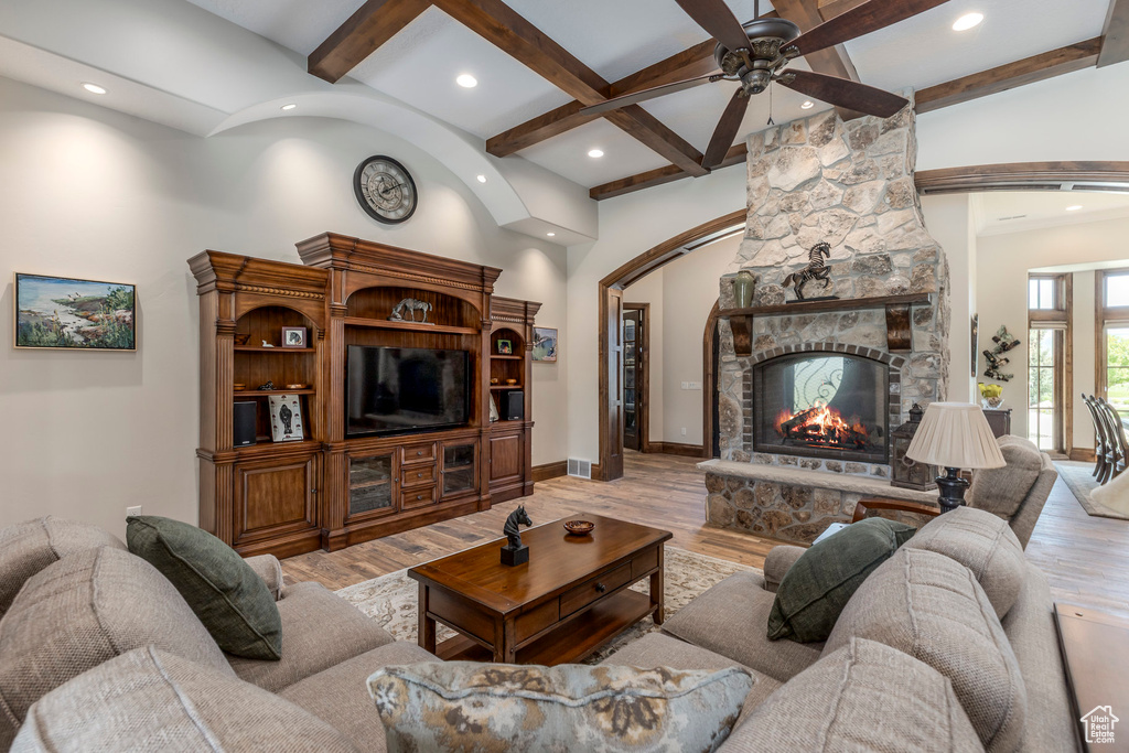 Living room with a stone fireplace, beamed ceiling, recessed lighting, ceiling fan, and light wood-type flooring