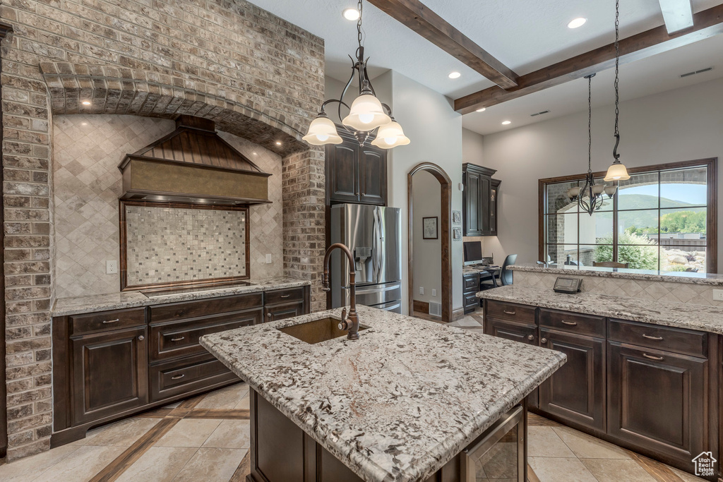 Kitchen with stainless steel refrigerator with ice dispenser, a sink, a chandelier, stovetop, and a center island with sink