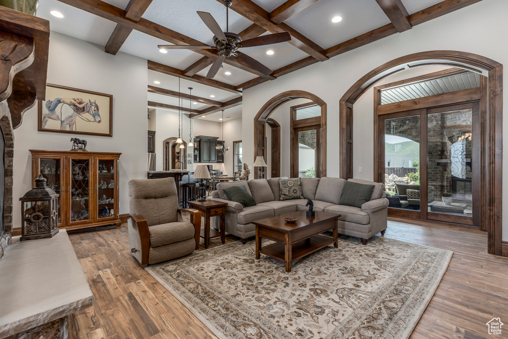 Living room with coffered ceiling, beamed ceiling, ceiling fan, arched walkways, and hardwood / wood-style flooring