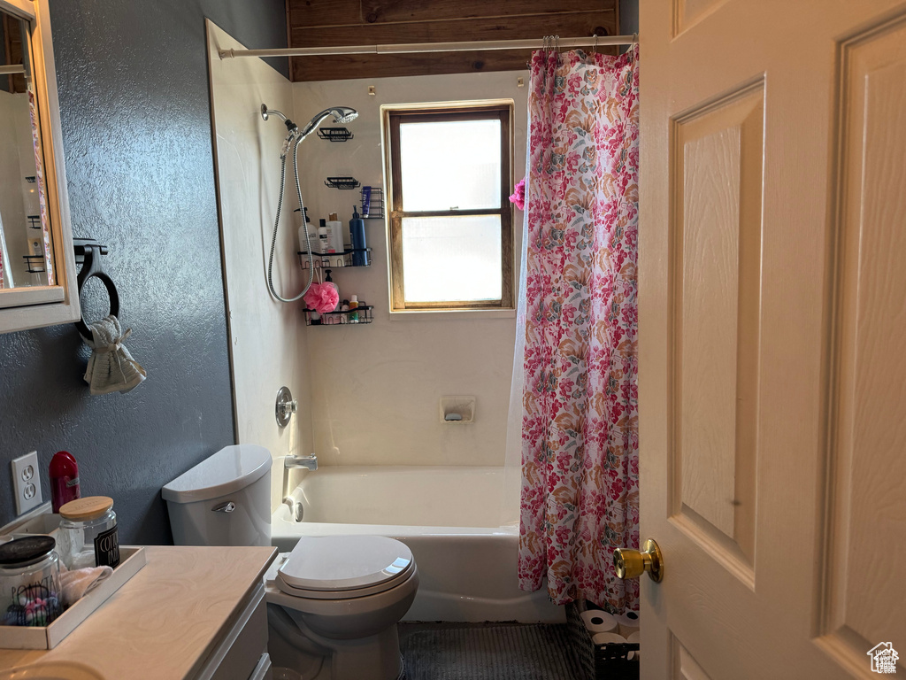 Bathroom with toilet, vanity, shower / bath combo with shower curtain, and a textured wall