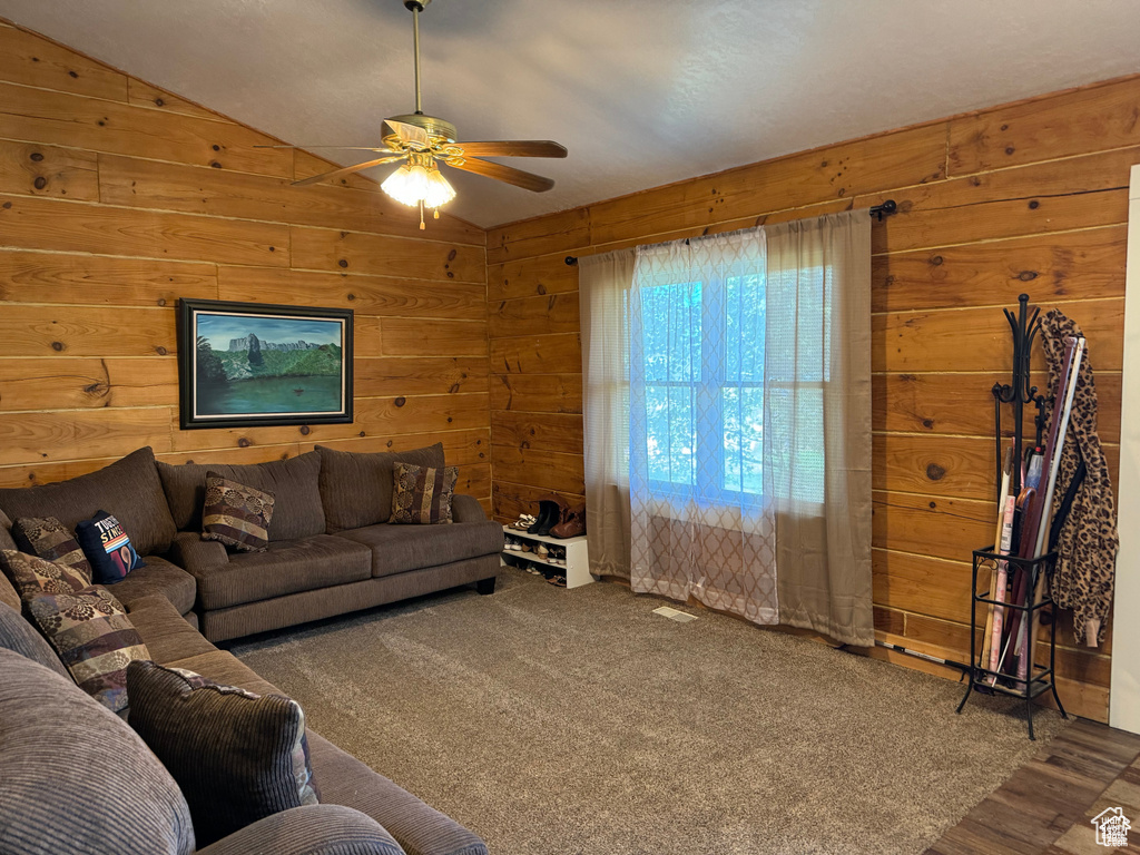 Living room featuring a ceiling fan, wooden walls, and vaulted ceiling