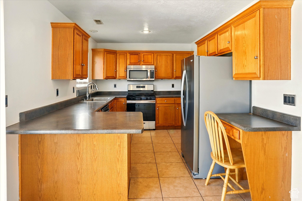 Kitchen with stainless steel appliances, a sink, dark countertops, a peninsula, and light tile patterned floors